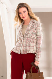 "Blonde Frau mit roter Hose und beige, leicht rotkarierten Blazer und Handtasche in der Hand."